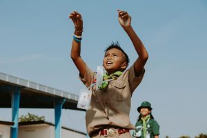 Un scout joyeux, les bras levés, jouant dehors par une journée ensoleillée.