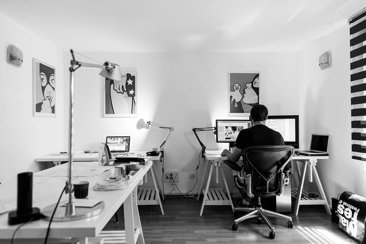 Homme assis devant un ordinateur dans un bureau avec deux lampes de bureau et des tableaux sur les murs Homme assis devant un ordinateur dans un bureau avec deux lampes de bureau et des tableaux sur les murs